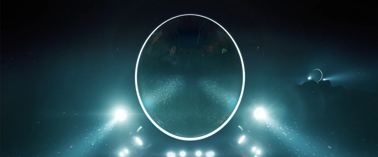 Meg 2: The Trench (2023) movie still: wide — A dark deep sea environment is illuminated by the powerful beams of a submarine. The submarine travels…