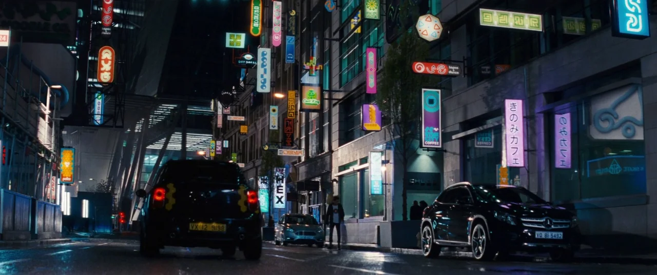 Pokémon Detective Pikachu movie still: wide — A dense urban street at night is illuminated by numerous vertical glowing neon signs. Two cars sit…