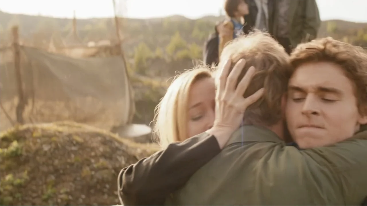 Robot Overlords (2015) movie still: medium — An open field at golden hour features a blurred background of distant low hills. A blonde woman and a…