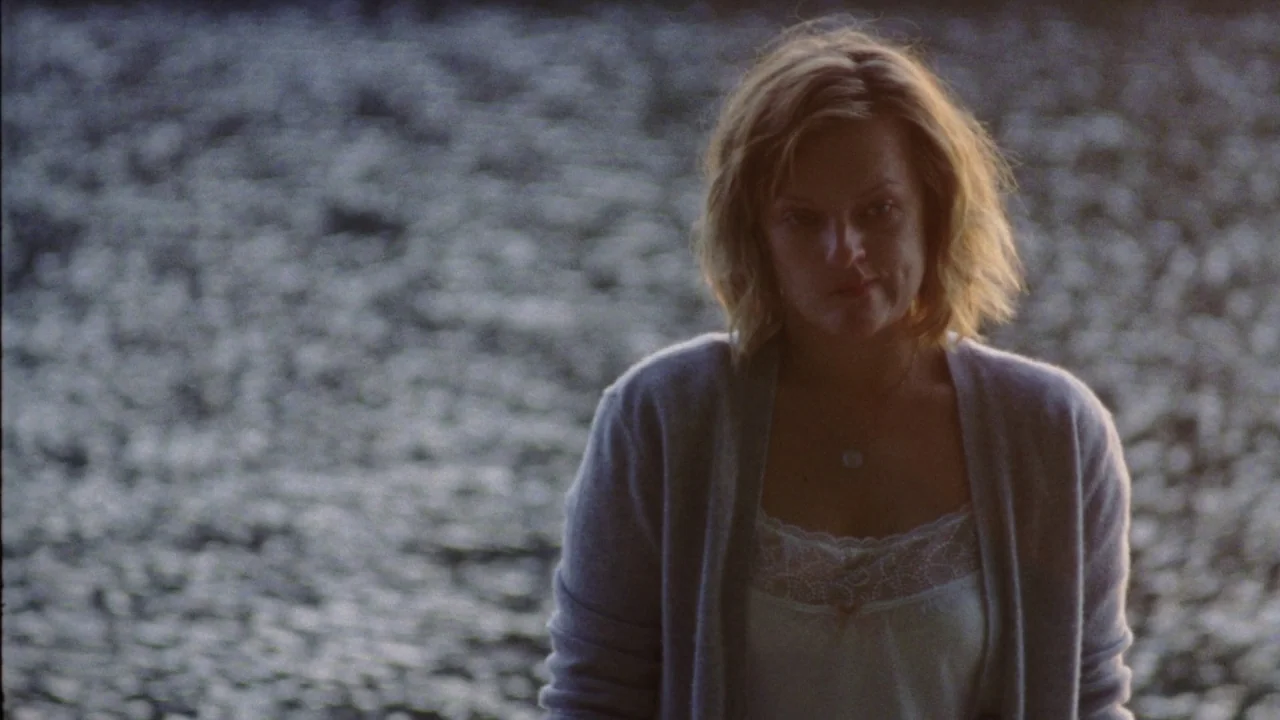 Queen of Earth (2015) movie still: medium — A woman stands before a dark, shimmering body of water at dusk. She is positioned against the…