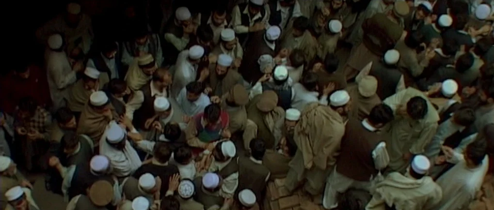 A Mighty Heart (2007) movie still: wide — A dense gathering of men in an outdoor space with brick ground textures. They are tightly packed together…