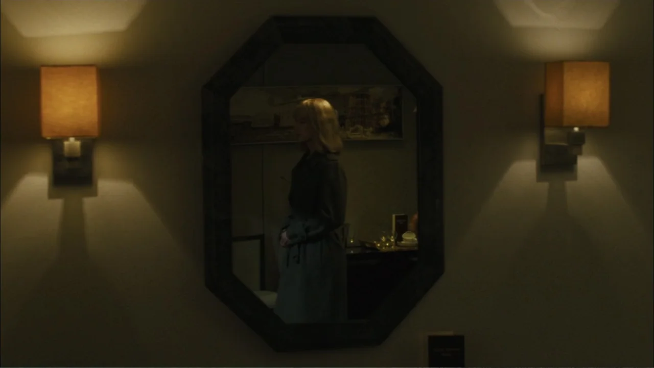 Before I Go to Sleep (2014) movie still: medium — A dark hotel room features two wall sconces illuminating a large octagonal mirror. A woman in a…