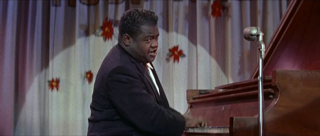 The Girl Can’t Help It (1956) movie still: medium — A man performs on a stage decorated with a curtain and holiday poinsettia patterns. He plays a…