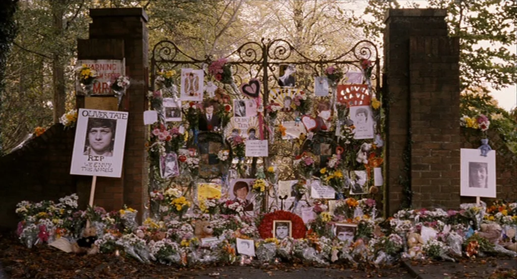 Submarine movie still: wide — A pair of decorative iron gates are covered in numerous memorial tributes and photographs. Piles of fresh flowers and…