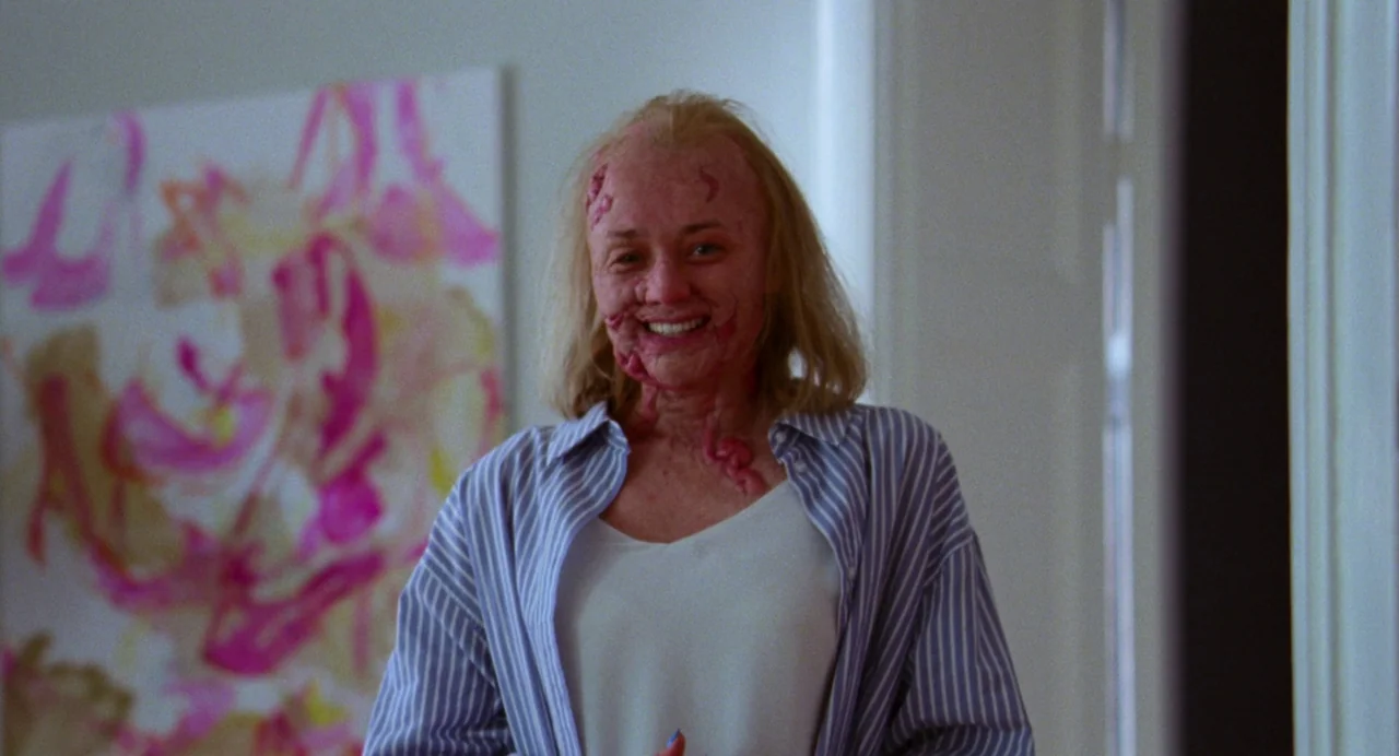 Sick of Myself (2022) movie still: medium — A residential hallway with white walls featuring an abstract pink painting. A middle-aged woman with…