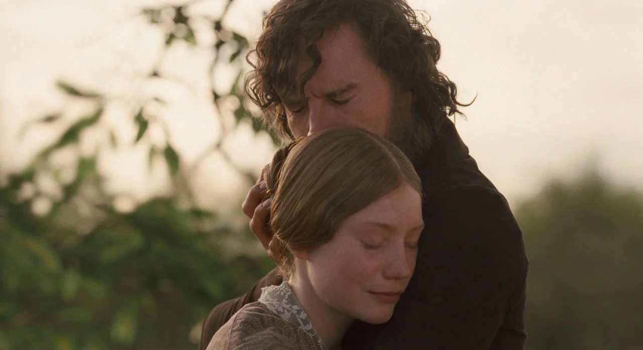 Jane Eyre (2011) movie still: closeup — An outdoor field during golden hour with soft warm light surrounding the figures. A man with long wavy hair…