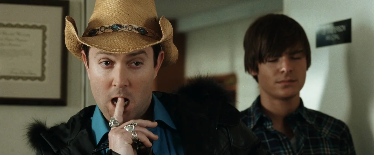 17 Again (2009) movie still: medium — A man in a straw cowboy hat stands in a brightly lit corridor. He holds a finger to his lips while another man…