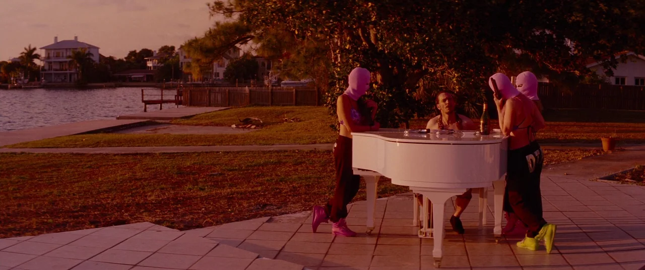 Spring Breakers (2012) movie still: wide — A suburban residential waterfront property features a white grand piano set on paved tiles. Three figures…