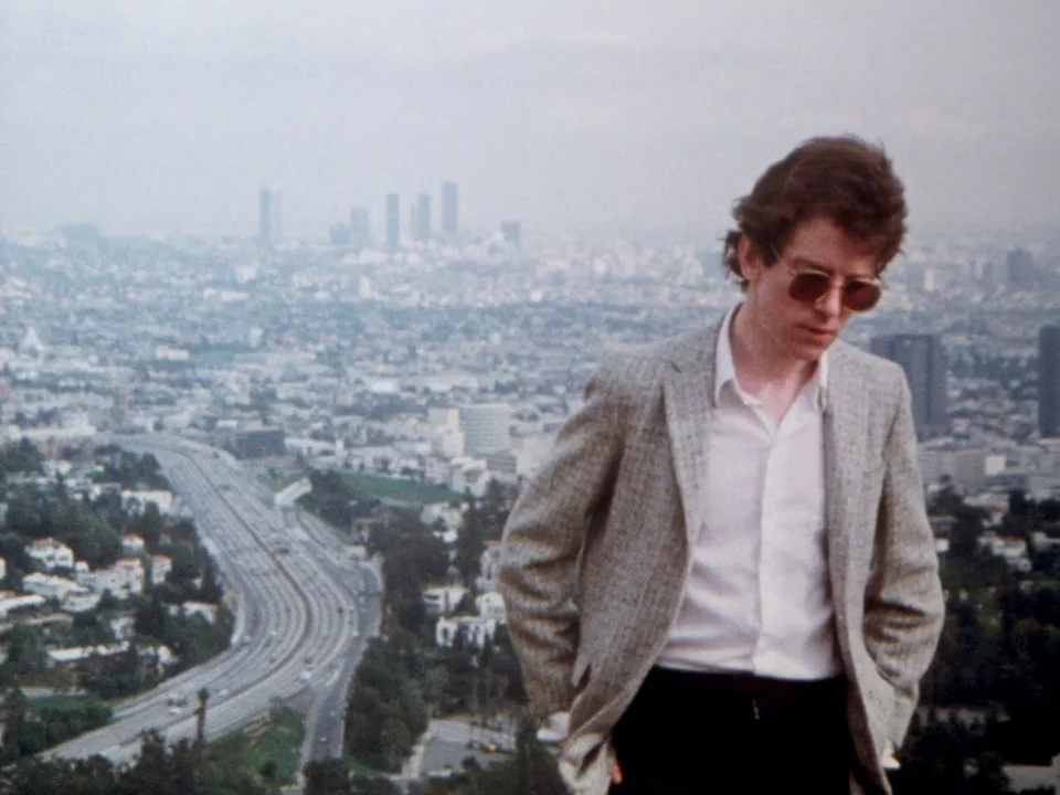 Decline of Western Civilization (1981) movie still: medium — A man stands on a hill overlooking a sprawling city and a winding highway. The city…