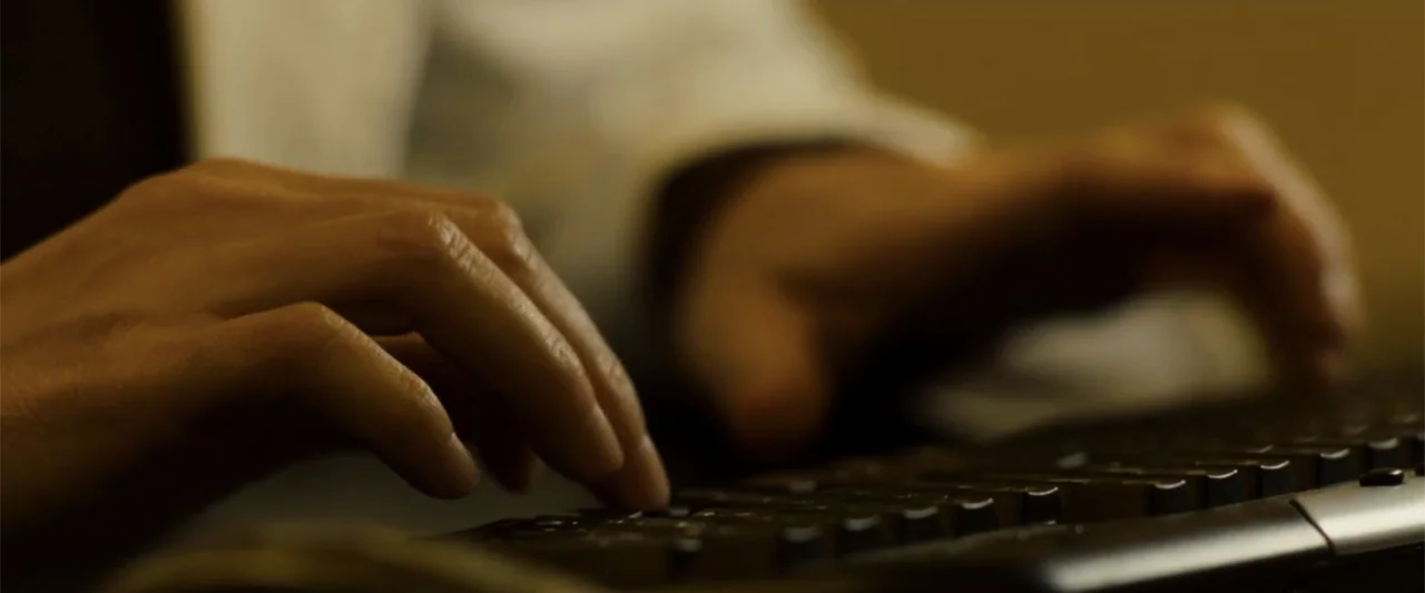 Angels & Demons (2009) movie still: closeup — An interior space with a person's hands positioned over a standard black keyboard. The fingers strike…