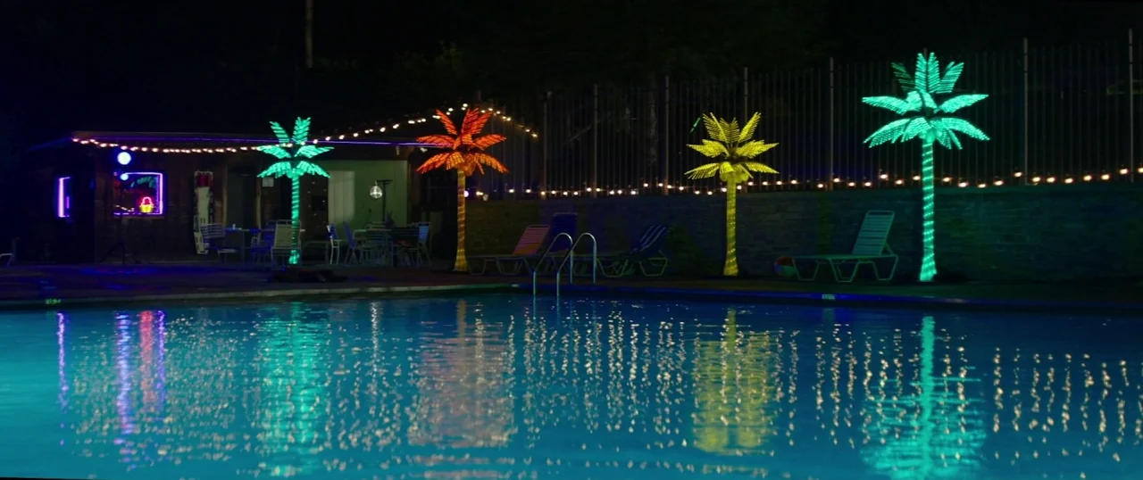 The Strangers: Prey at Night (2018) movie still: wide — An outdoor pool at night surrounded by a stone wall and metal fencing. Illuminated…