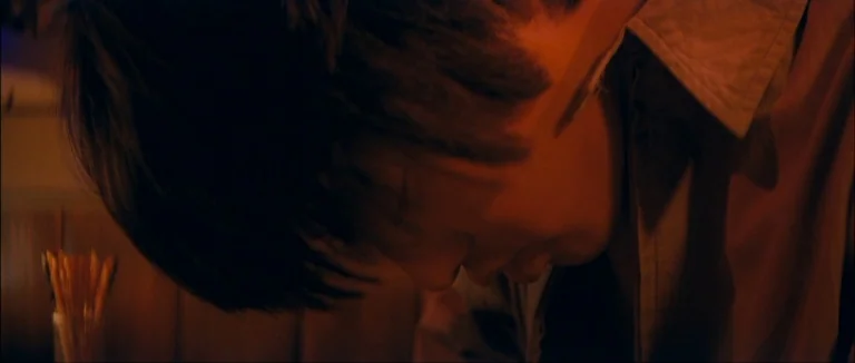 Mother (2009) movie still: closeup — A dimly lit restaurant booth features warm lighting on a seated man. A man with dark hair leans his head…