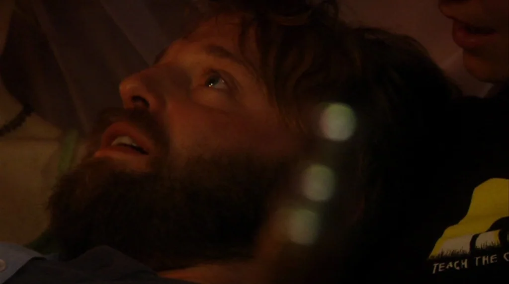 Humpday (2009) movie still: closeup — A dimly lit room with shadows obscuring most details of the surroundings. A man with a thick beard lies on his…