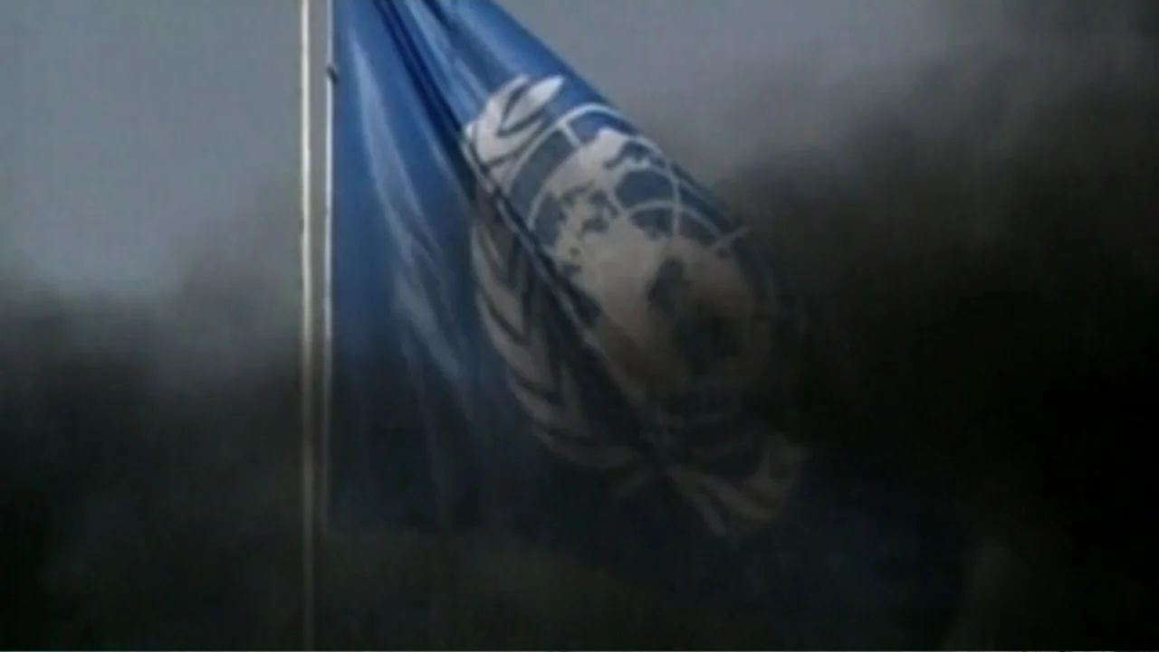 Ghosts of Abu Ghraib (2007) movie still: medium — A blue United Nations flag flies from a metal pole through thick dark smoke. The flag remains…