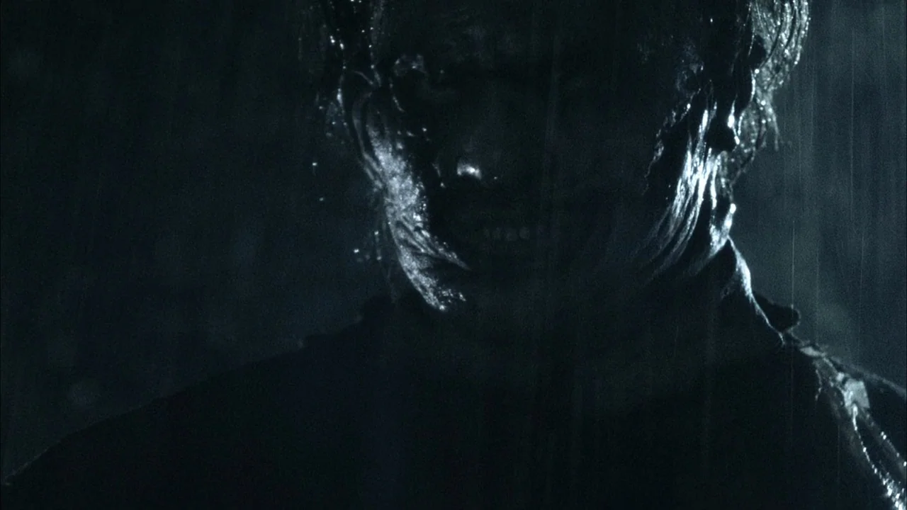 The Texas Chainsaw Massacre (2003) movie still: closeup — A dark environment at night with heavy rain streaks visible against a black background. A…