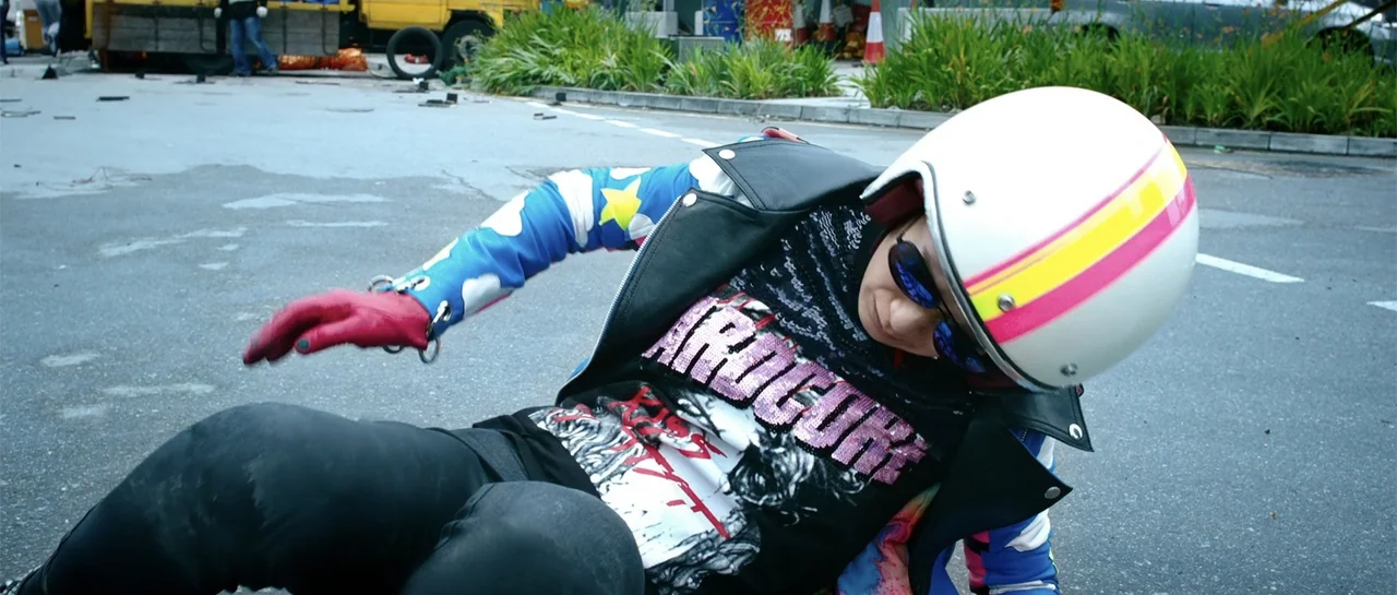 Line Walker (2016) movie still: medium — An asphalt parking lot has white painted lines and sparse vegetation in the background. A person wearing a…