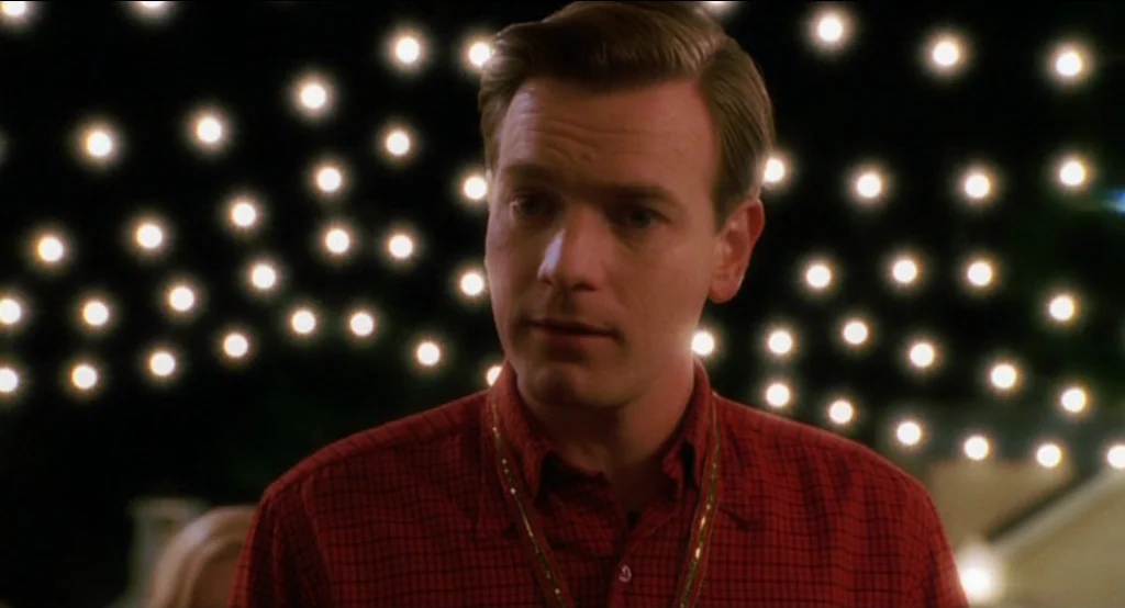 Big Fish (2003) movie still: medium — A man stands outdoors at night in front of a wall of string lights. The bright points of light create a bokeh…