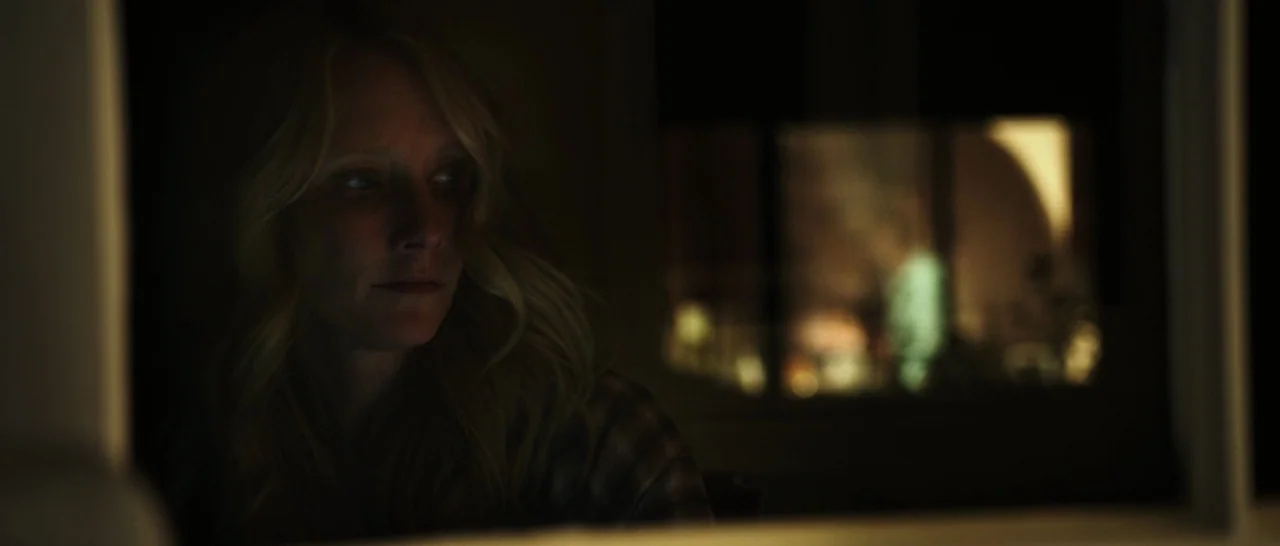 Rampart (2011) movie still: closeup — A dimly lit room with a woman viewed from a close distance. The woman sits while looking away from the camera…