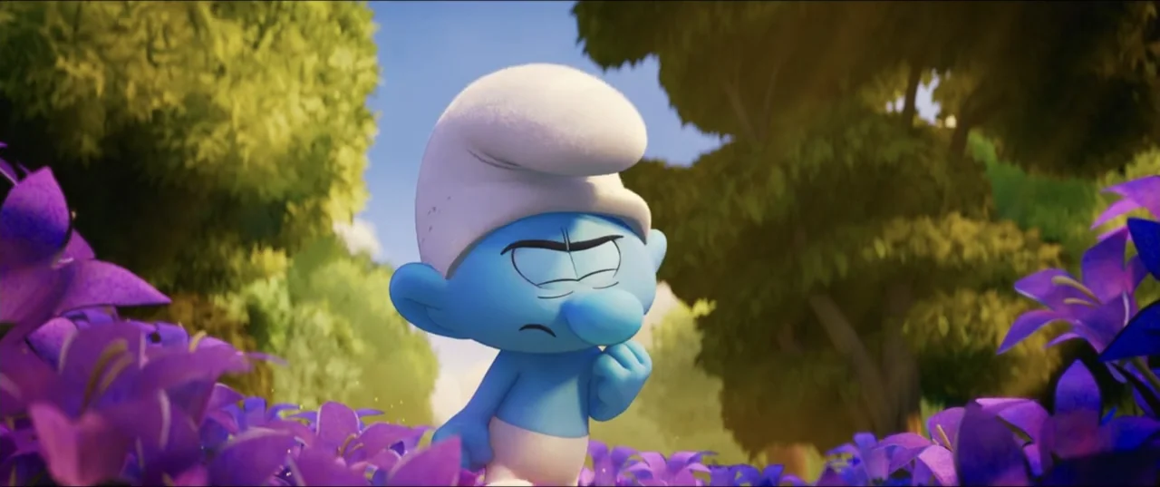 Smurfs (2025) movie still: medium — A sunny field filled with purple bell-shaped flowers and dense green trees. A small blue character stands amidst…