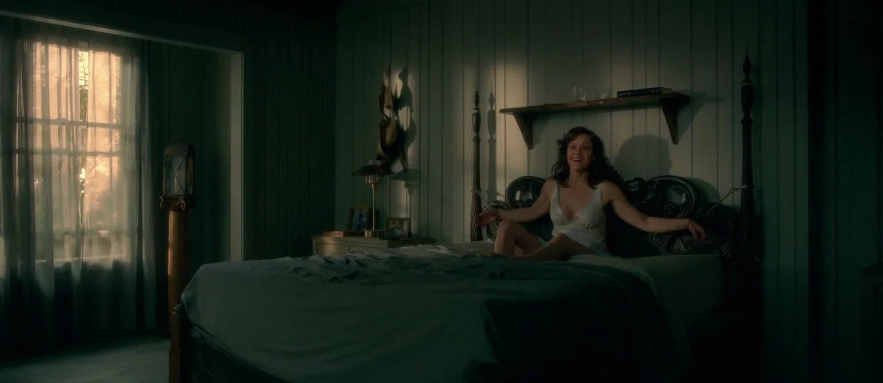 Gerald’s Game (2017) movie still: medium — A dark, wood-paneled room contains a large bed with a dark ornate headboard. A woman with dark hair sits…