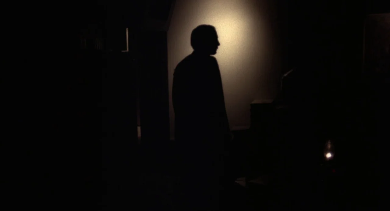 The Killing of a Chinese Bookie (1976) movie still: fullbody — A dark, dimly lit room features a single pool of light on the wall. A man stands in…
