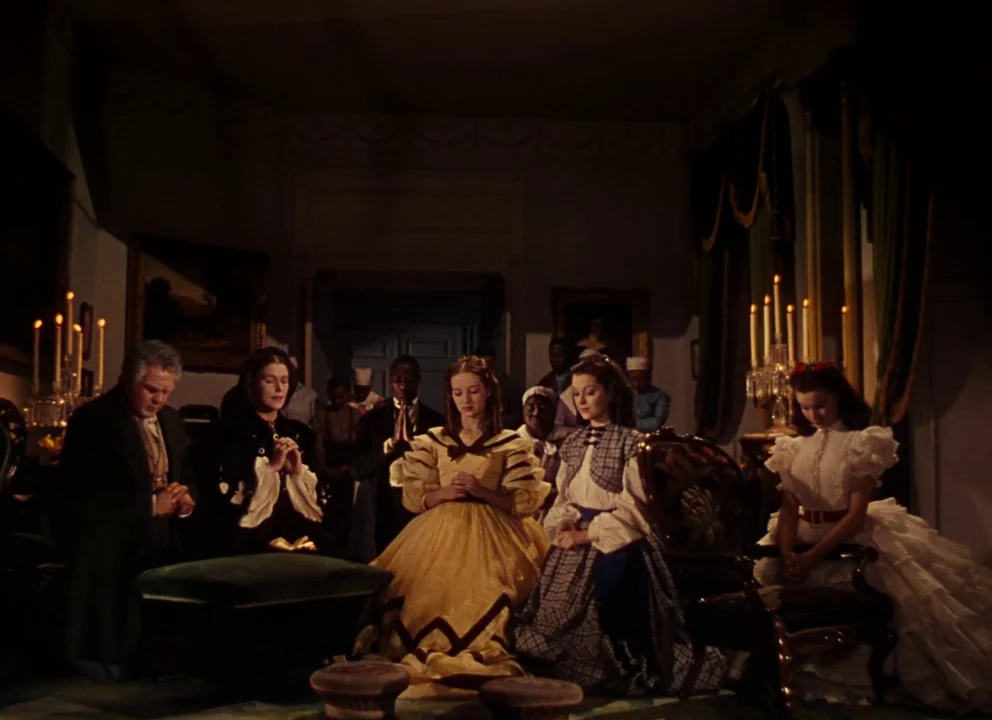 Gone with the Wind (1939) movie still: wide — An opulent 19th-century parlor is dimly lit by candles held in silver candelabras. A group of people…