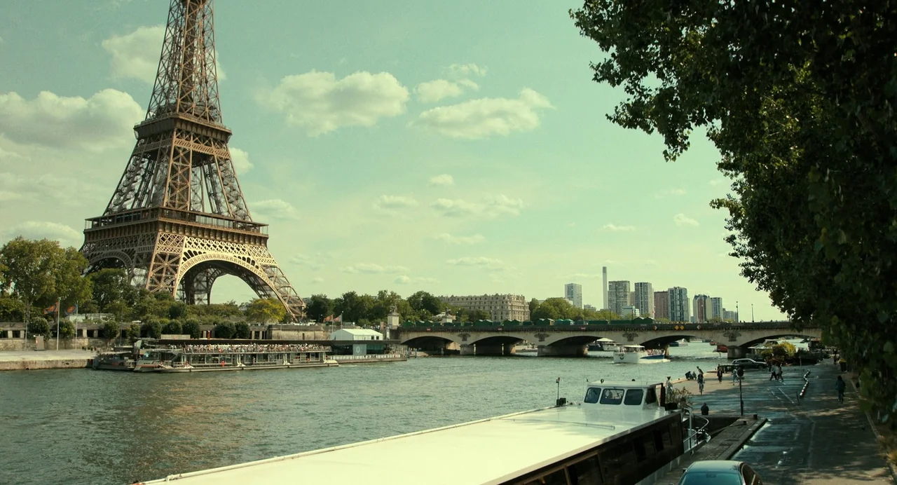 The Killer (2024) (2024) movie still: establishing — The Eiffel Tower stands prominently along the Seine river in a sunlit urban setting. A tour…