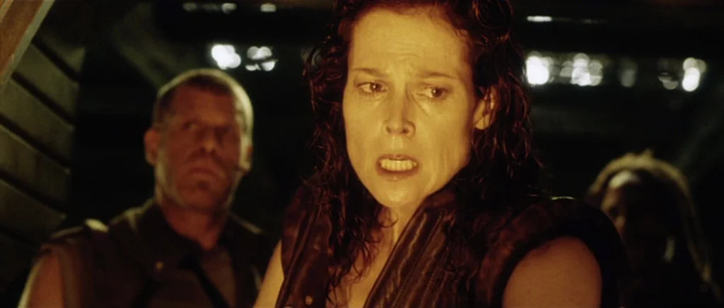 Alien: Resurrection (1997) movie still: medium — A dark, cramped corridor inside a spaceship with metallic walls. A woman with wet hair looks…