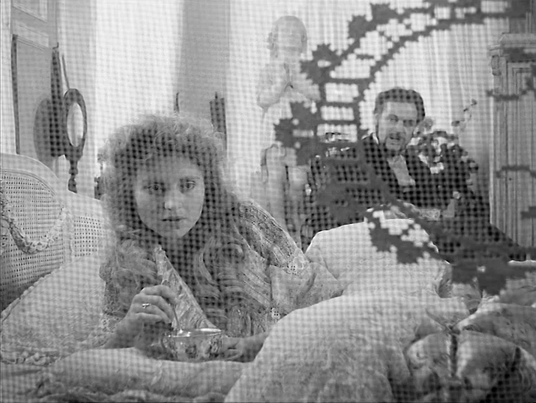 Effi Briest (1974) movie still: medium — A ornate bedroom is viewed through a decorative lace screen or mesh. A woman rests on the bed with a tea…