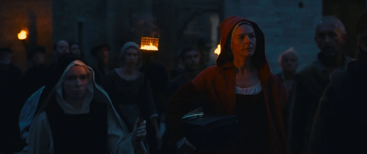 Benedetta (2021) movie still: medium — A group of medieval people walk through a dark village at night. The foreground women carry torches and a…