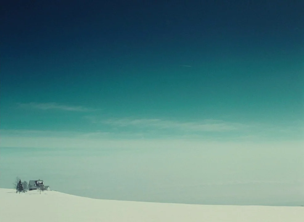 Laurence Anyways (2012) movie still: establishing — A remote house sits atop a snowy incline against a vast, clear blue sky. The environment is…