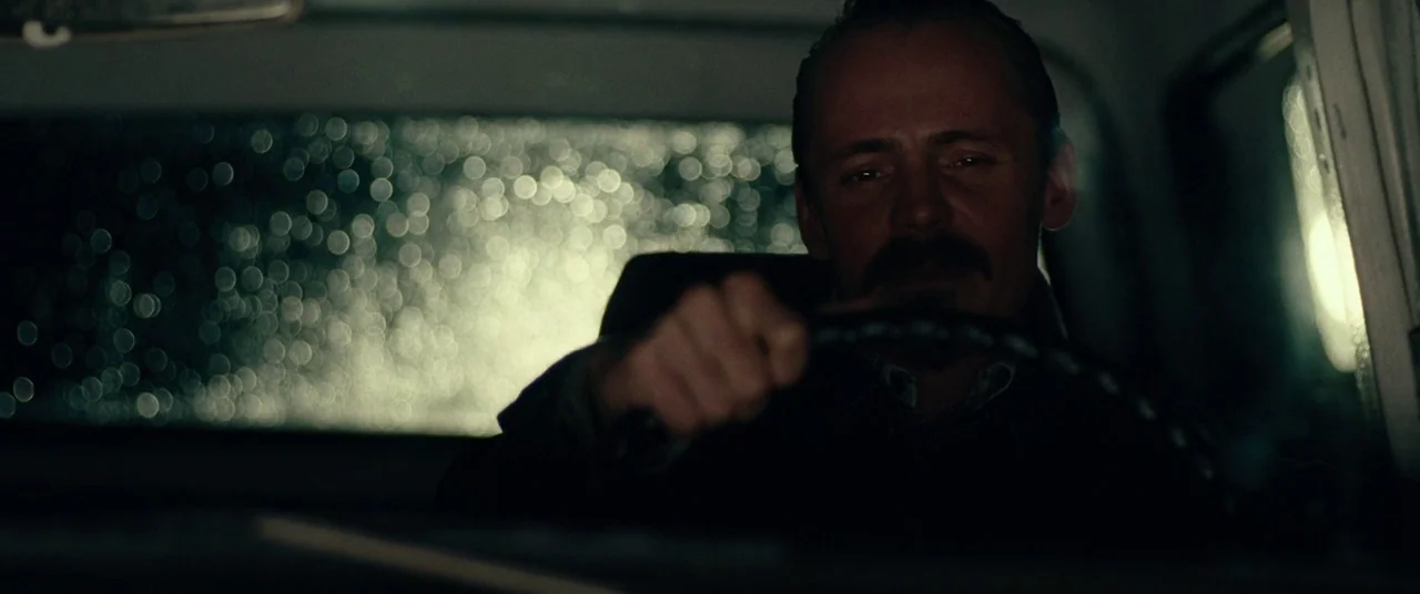 BlacKkKlansman (2018) movie still: medium — A man drives a vehicle at night during a rainstorm. Raindrops blur the light from the back window.