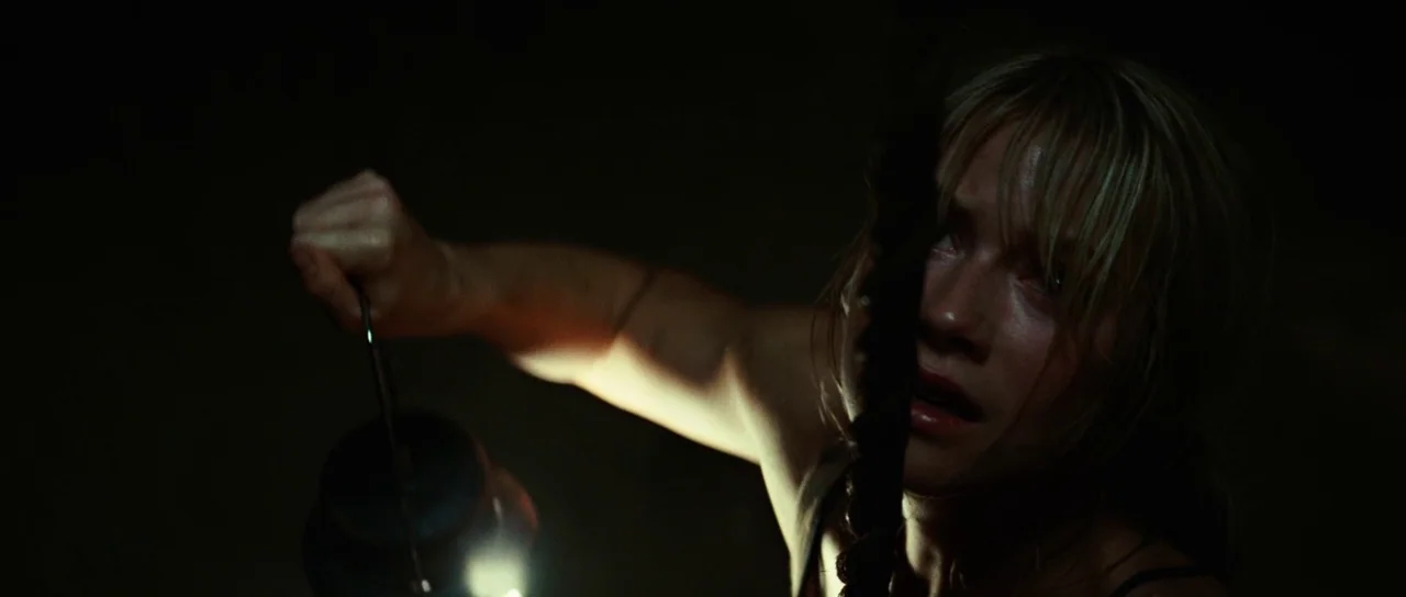 The Ruins (2008) movie still: closeup — A dark, undifferentiated space features only the subject illuminated by a small lantern. The subject holds…