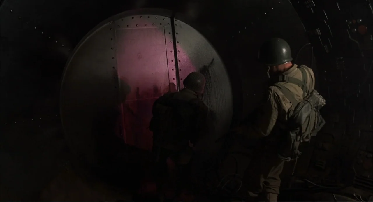 Zone Troopers (1985) movie still: medium — A dark, cramped corridor features curved metal walls with visible rivets and bolts. Two soldiers in…