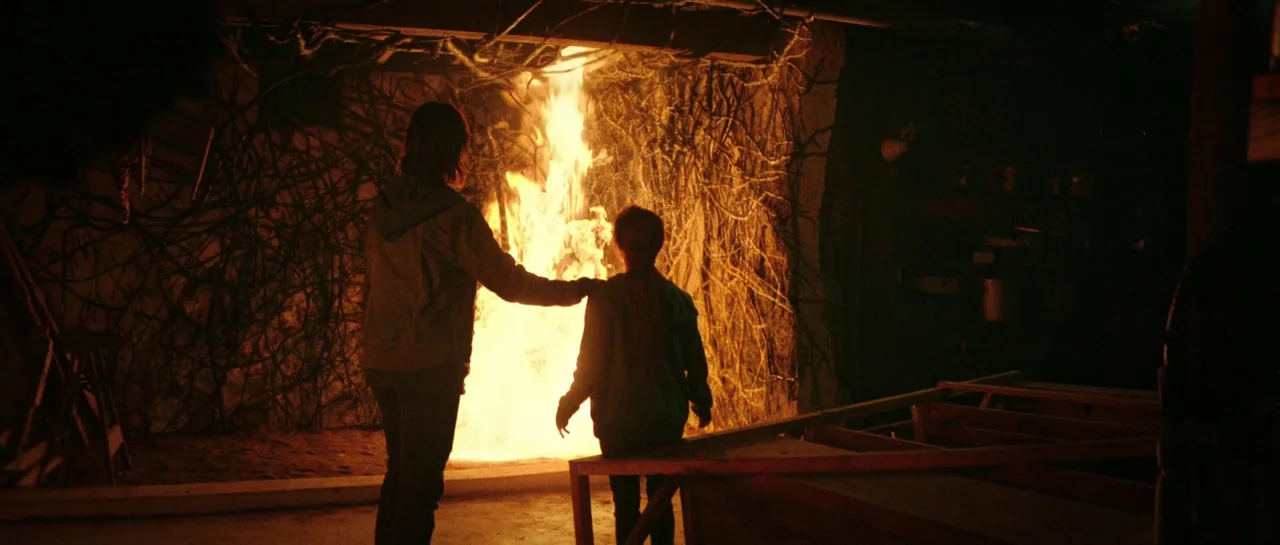 The Boogeyman (2023) movie still: fullbody — A dark, unfinished basement with exposed wooden beams and walls covered in dark vines. A large fire…