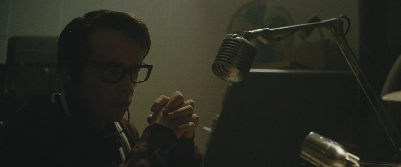 The Vast of Night (2019) movie still: medium — A dimly lit room contains radio broadcasting equipment and a professional metal microphone. The man…