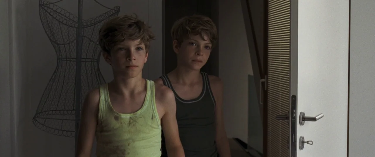 Goodnight Mommy (2014) movie still: medium — A modern hallway interior contains a metal dress form frame and a white door. Two young twin boys stand…
