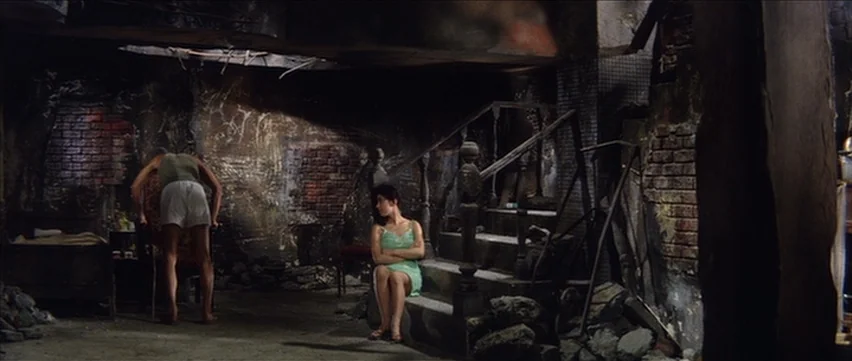 Gate of Flesh (1964) movie still: wide — A dilapidated, bomb-damaged room features exposed brick walls, debris piles, and a central staircase. A man…