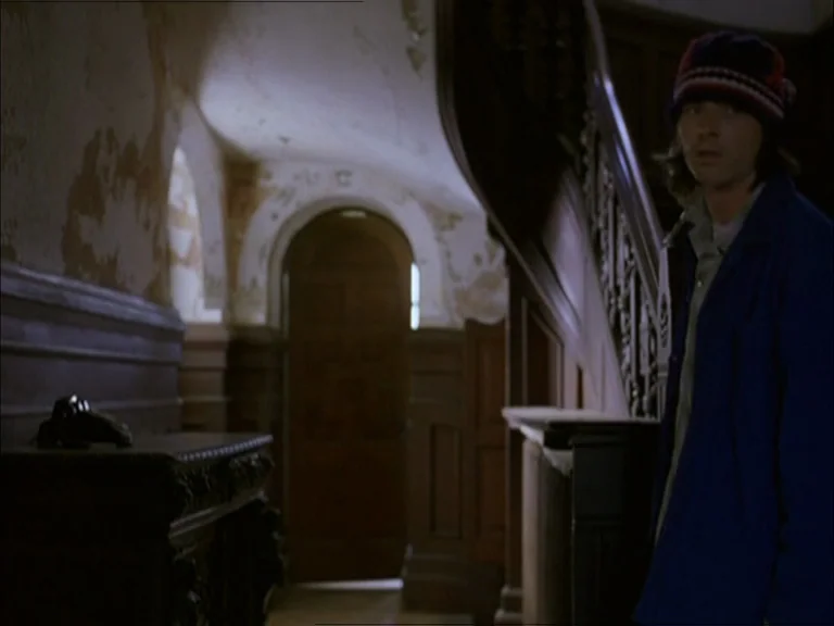 Last Days (2005) movie still: medium — A dimly lit entryway features peeling plaster walls and a dark wooden staircase. A man stands in the…