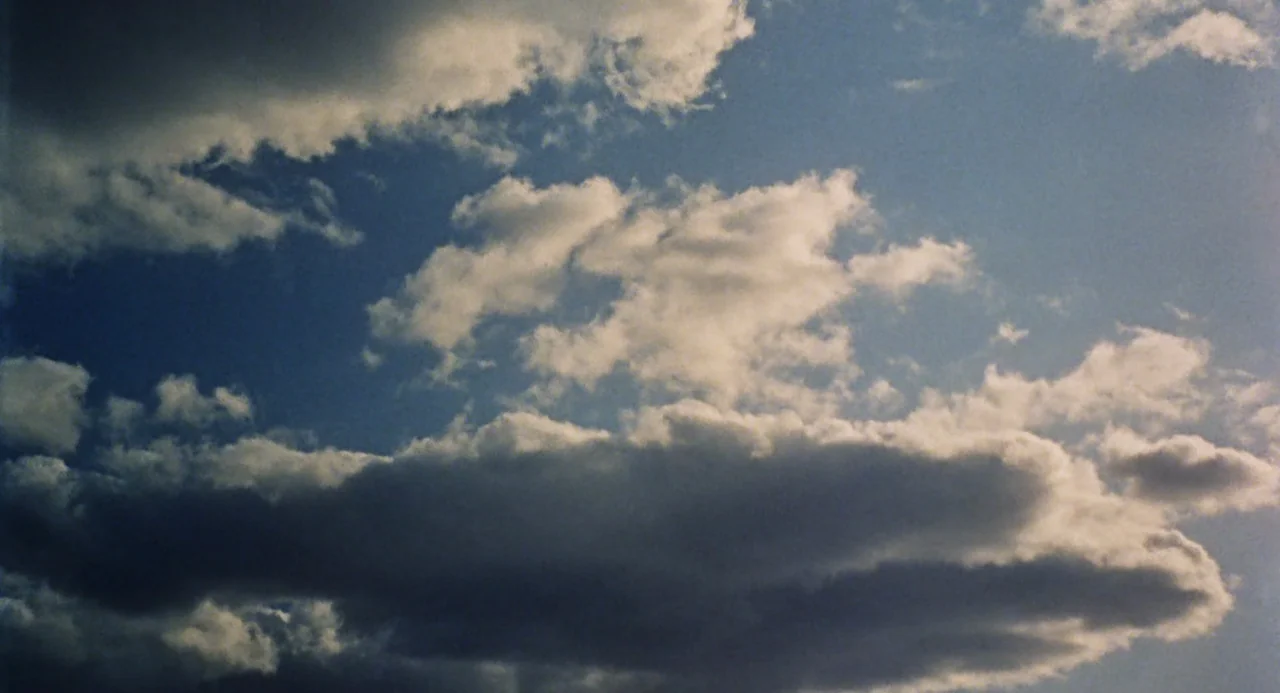The Swimmer (1968) movie still: establishing — A patch of blue sky is partially obscured by thick, layered cumulus clouds. The sunlight creates…