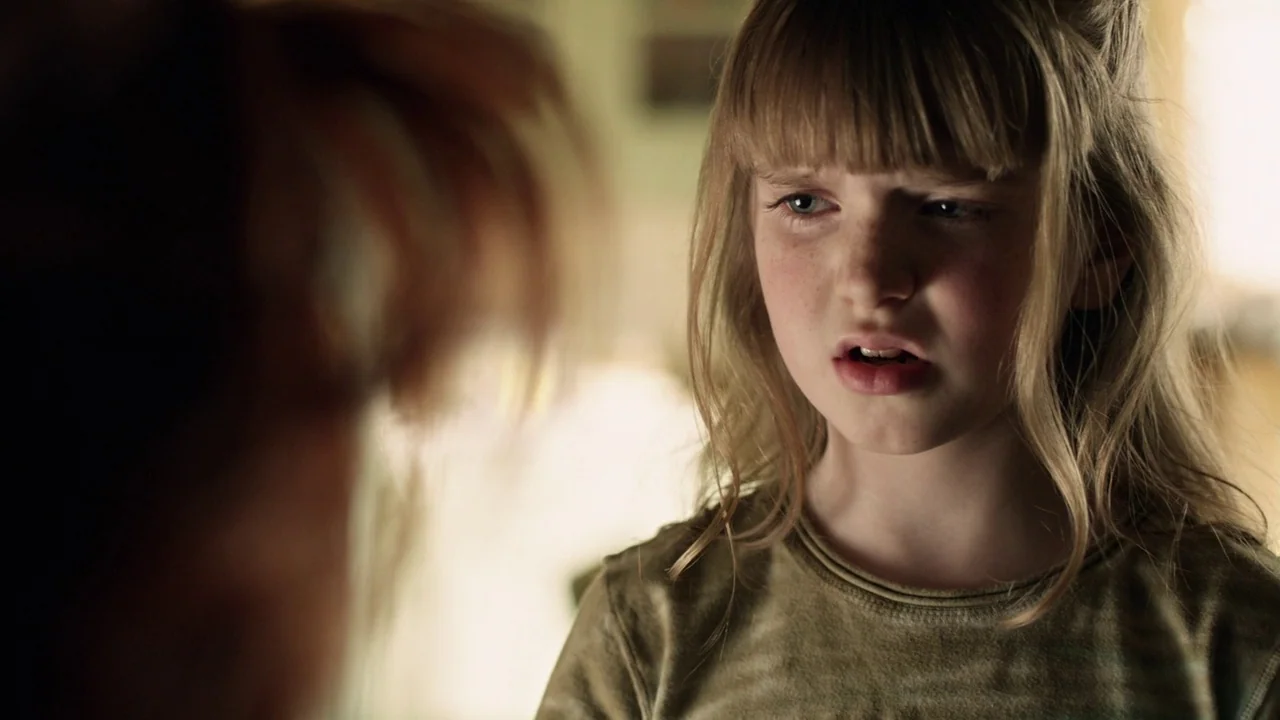Curse of Chucky (2013) movie still: closeup — A close-up captures a young girl in a brightly lit domestic interior. She looks toward another person…
