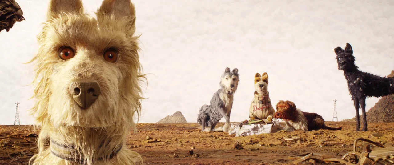Isle of Dogs (2018) movie still: wide — A vast, desolate landscape filled with scrap metal and debris under a cloudy sky. Five dogs of various…