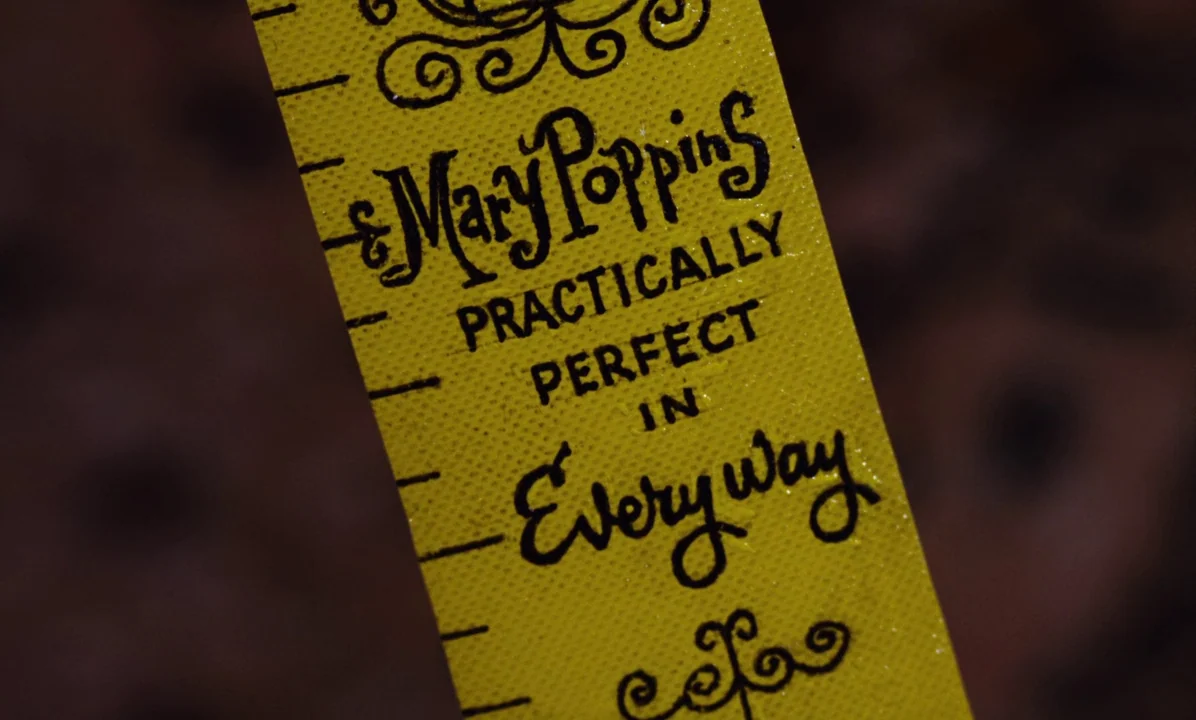 Mary Poppins (1964) movie still: closeup — A close-up shot of a bright yellow fabric measuring tape with black text. The text displays Mary Poppins…