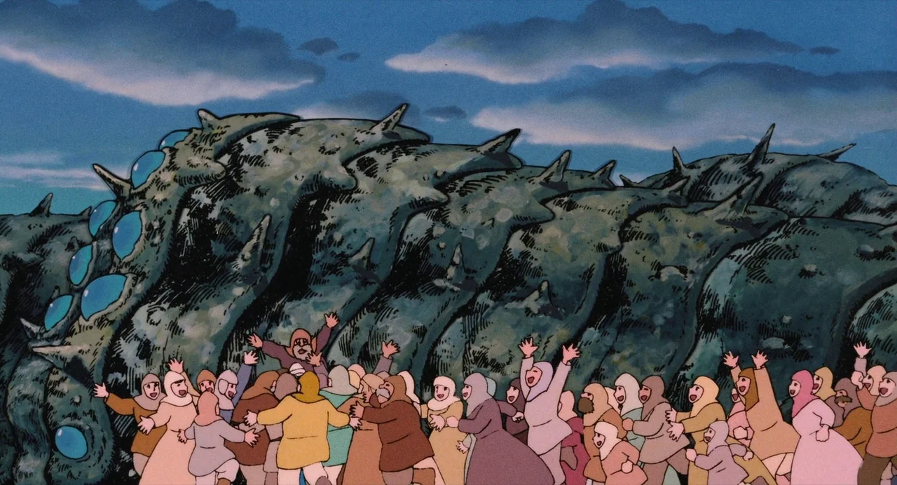 Nausicaä of the Valley of the Wind (1984) movie still: wide — A crowd of people in hooded cloaks stands before a massive, multi-eyed segmented…