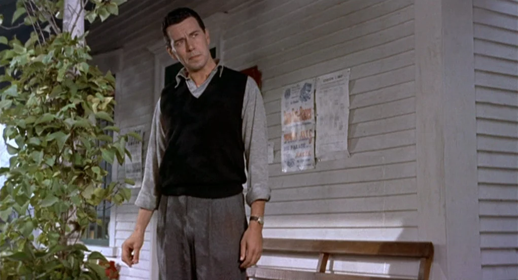 The Trouble With Harry (1955) movie still: fullbody — A wooden porch with white clapboard siding and posted paper signs. A man stands near a leafy…