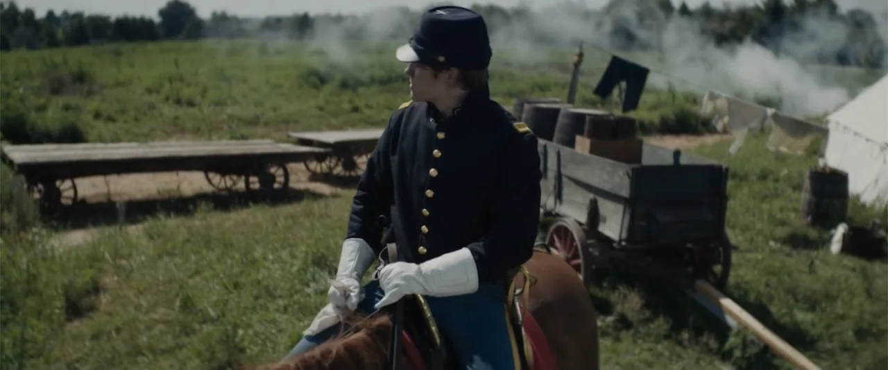 I Heard the Bells (2022) movie still: medium — An open field containing an encampment with a wooden wagon and white canvas tents. A Union soldier in…