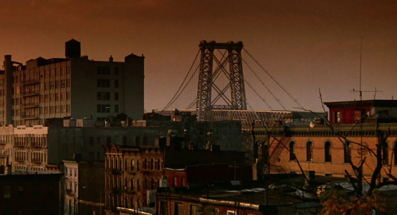 Jacob’s Ladder (1990) movie still: establishing — A dense urban landscape features brick apartment buildings under a warm orange dusk sky. The…