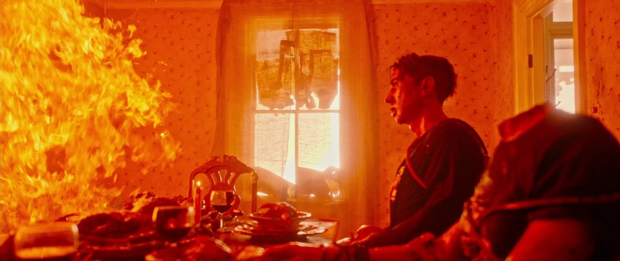 Random Acts of Violence (2019) movie still: medium — A dining room features floral wallpaper and a table set with food and drinks. A person sits…