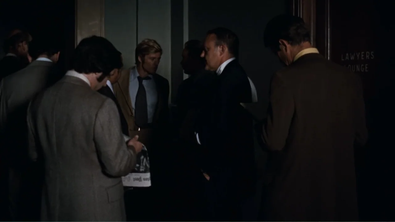 All the President's Men (1976) movie still: medium — A dimly lit indoor corridor with a sign on the door marked Lawyers Lounge. Several men in…