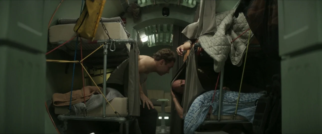 Last Breath (2025) movie still: medium — A cramped, metallic cabin interior contains stacked bunk beds with industrial piping and frames. A…